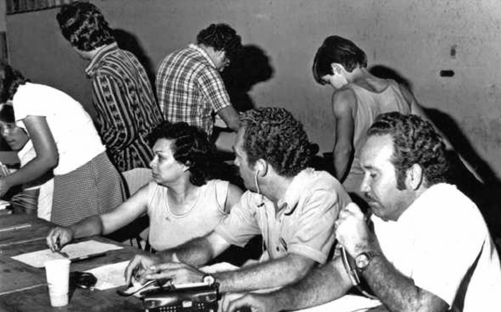 Em ação a equipe da Rádio Clube AM na cobertura da apuração dos votos na eleição de 1976. Naquele pleito eleitoral, o dentista João Antonio Nucci elegeu-se prefeito pela primeira vez. O radialista Aguinaldo de Oliveira (à direita com o microfone) foi eleito o vereador mais votado com 768 votos pela Arena. Na esquerda, o técnico de som Shoyo e na mesa o casal de radialistas Luiz Rivoiro e Oneide Aparecida Lourenço Rivoiro. Atrás, de costas, Edélcio Martins e Celso Fiorentino.
