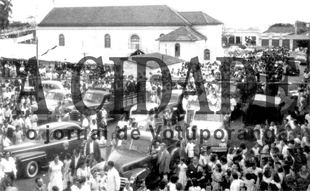 O dia 13 de Maio é consagrado a Nossa Senhora de Fátima, de origem em Portugal. Uma réplica da imagem percorreu o Brasil nos anos 50 e Votuporanga deu uma grande demonstração de fé e louvor à Virgem de Fátima. A imagem foi recebida pela população na rodovia, e entrou na cidade numa grande procissão. Na foto, o momento que a imagem deixava a velha Igreja na praça (hoje em frente à Catedral). Consta que num dos caminhões seguiam os Congregados Marianos e no outro as Filhas de Maria. Veja entre a multidão os carros da época, o Fordinho e o Studebaker, entre outros. Observe também ao lado da Igreja velha (onde hoje está a Fonte Luminosa, da Praça Fernando Costa) a barraca em que aconteciam as tradicionais quermesses. Ao fundo (nesta foto) dá para identificar também o prédio da antiga Rodoviária e o Armazém de César Beretta pela rua São Paulo. Uma foto histórica.