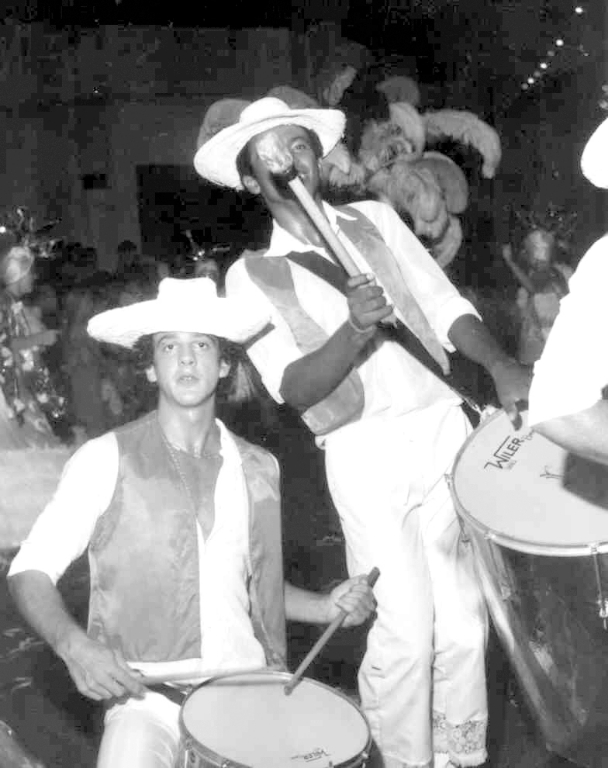 Na passarela do samba da rua Amazonas o destaque é para a ala da bateria do Grêmio Recreativo Escola de Samba Mulata Dengosa. A Mulata foi a escola que mais tempo permaneceu na ativa no carnaval de Votuporanga. Nesta foto, em primeiro plano aparece Rubens Grisi Junior ao lado de um batuqueiro não identificado pelos nossos colaboradores. A foto é do fotógrafo Rubens Grisi – pai do batuqueiro.