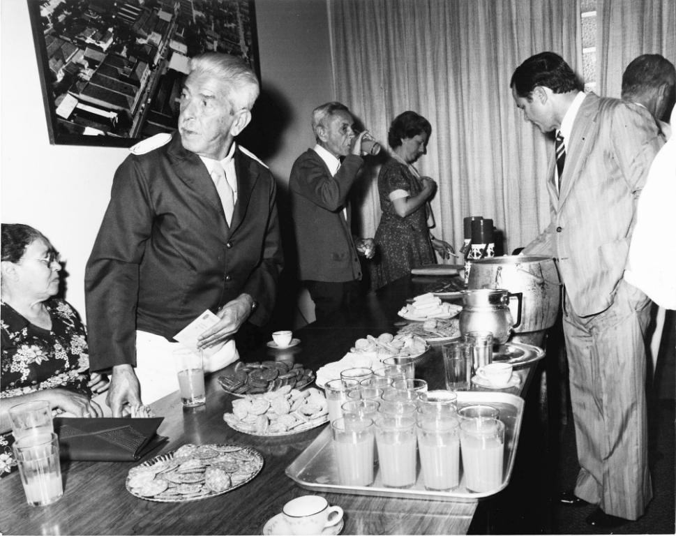 A foto é dos anos 70, da administração do prefeito João Antonio Nucci (1/02/77 a 31/01/83 – na primeira administração). Nesse período, ele institui a Medalha “8 de Agosto” que homenageava cidadãos que se revelavam no campo benemérito. Após o ato solene de homenagem era servido um coquetel. Aparece em primeiro plano José Alcebiades dos Santos, que comandava a corporação musical “Zequinha de Abreu”. Na direita estão o sargento Atiliano Guatemozim Pedroso e o vereador Alzimiro Brantis (primeiro prefeito de Parisi) , entre outros.