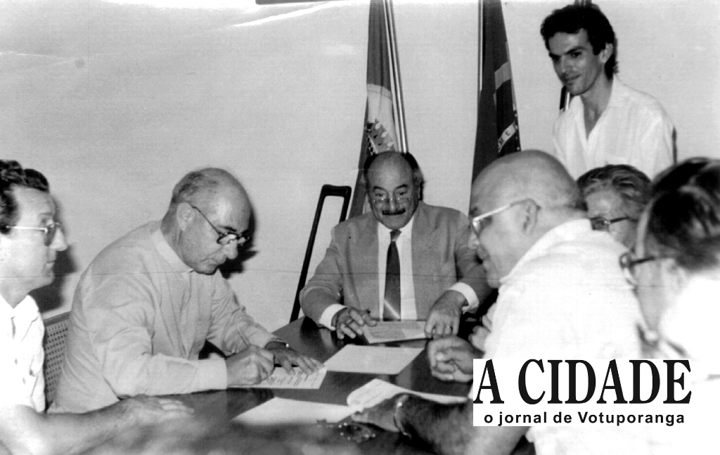 Ano 85 - O Bispo Diocesano de Rio Preto, D. José de Aquino Pereira, aparece nesta foto assinando documentos relativo a sessão de uma área por parte da Prefeitura à Igreja. Aparecem na foto, a partir da esquerda: Antonio Domingo Barbon, Bispo D. José, o então prefeito Mário Pozzobon, o assessor Luciano Viana (de pé) e o vereador Meidão, entre outros.